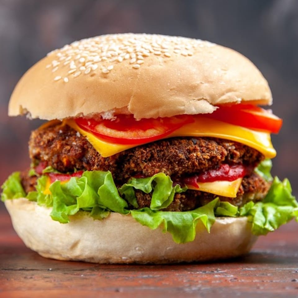 A large, double-patty burger with cheese, lettuce, and tomatoes on a sesame seed bun.