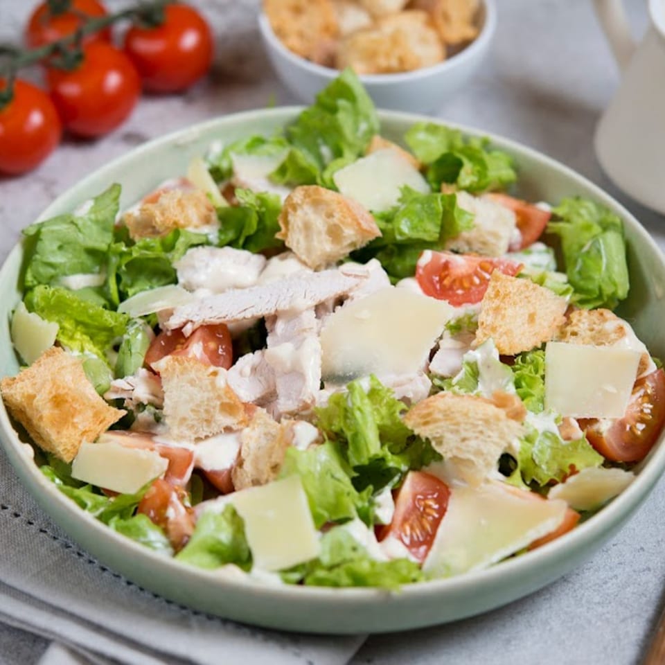 A Caesar salad with chicken, croutons, parmesan, and tomatoes in a light green bowl.