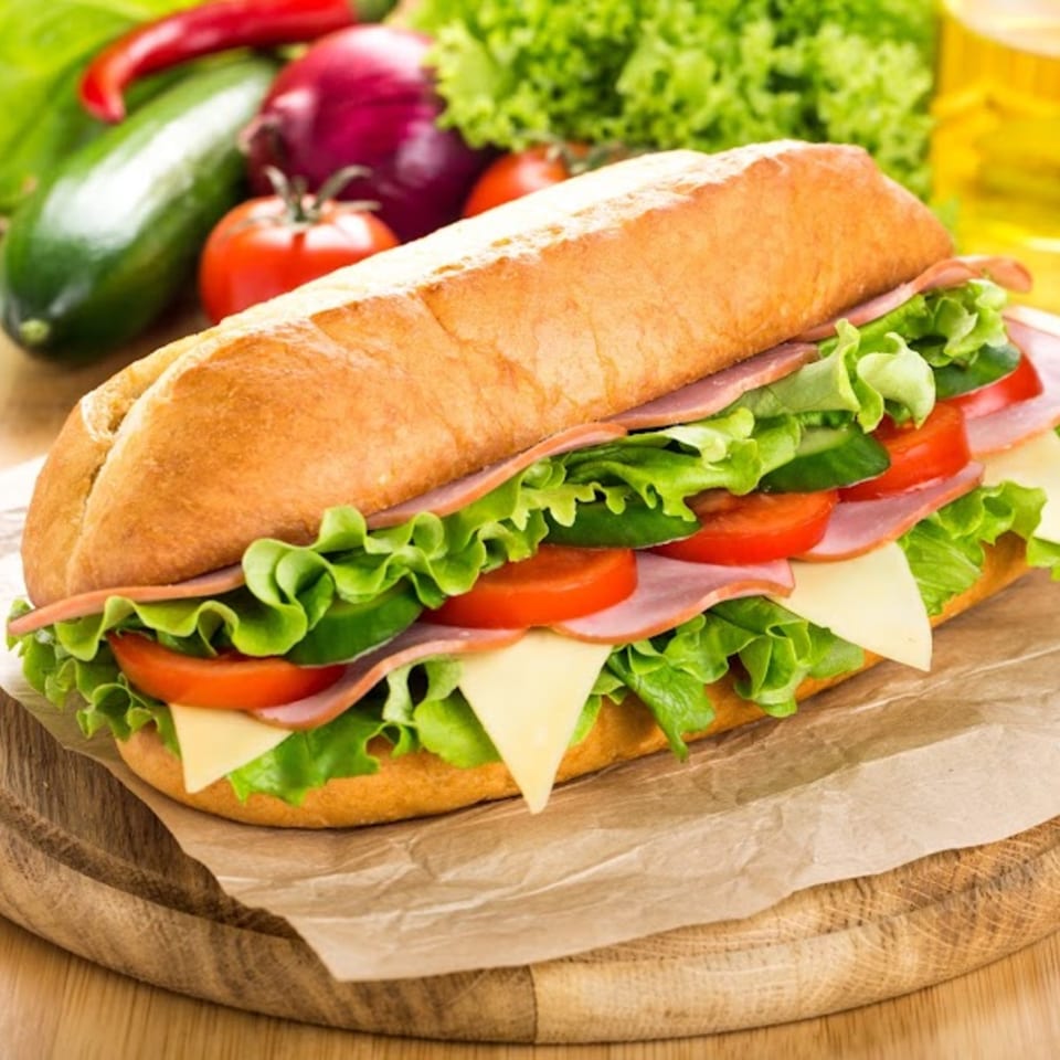 A large submarine sandwich with ham, cheese, lettuce, and tomatoes on a wooden board.